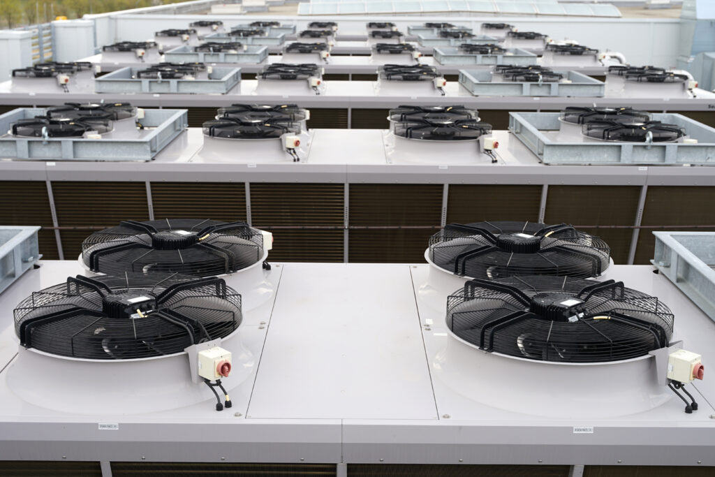 Large row of industrial condensers with fans on roof used in air conditioning, refrigeration, heat pump systems, renewable green energy future concept